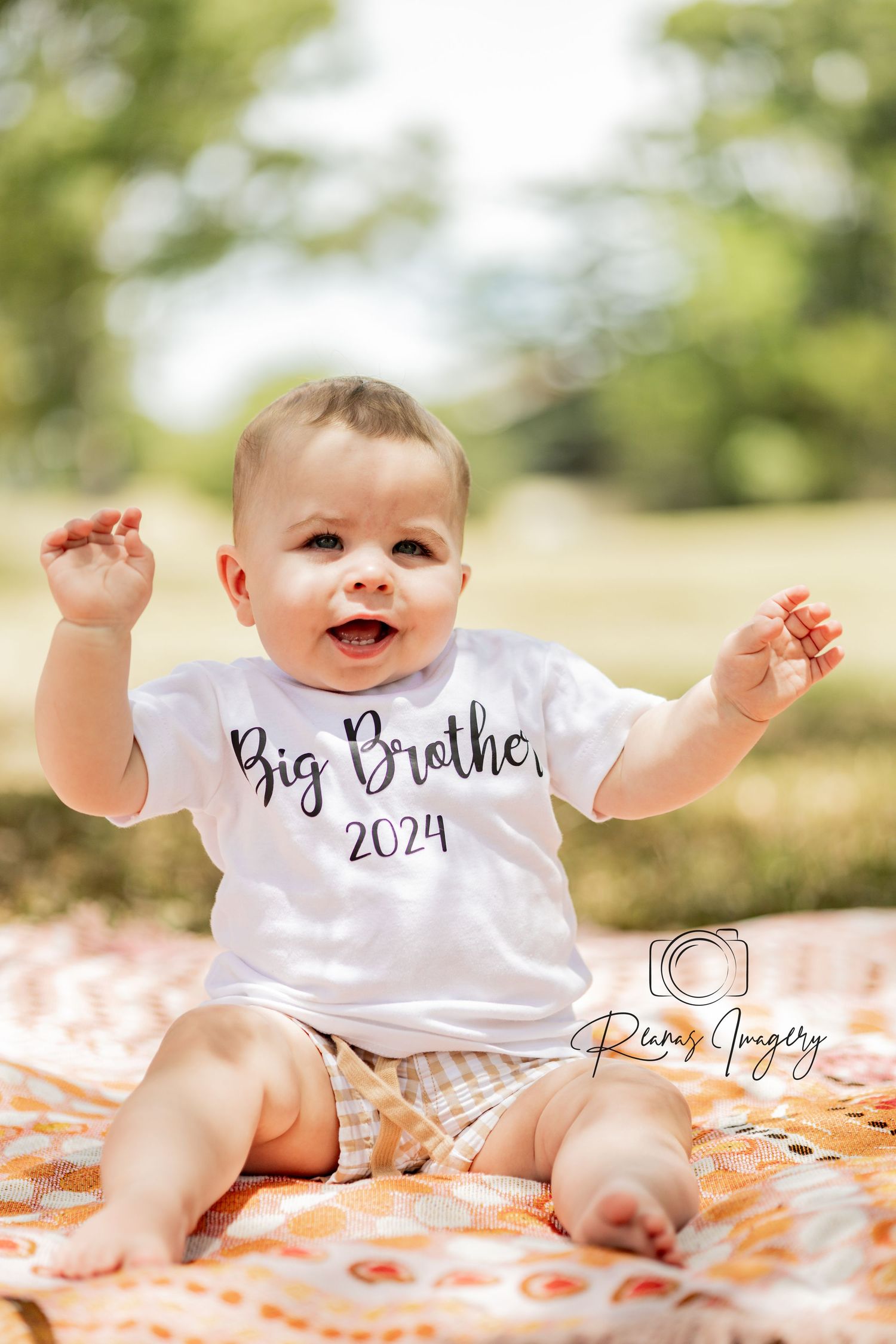 Happy baby boy sitting outdoors wearing a Big Brother 2024 white t-shirt.
