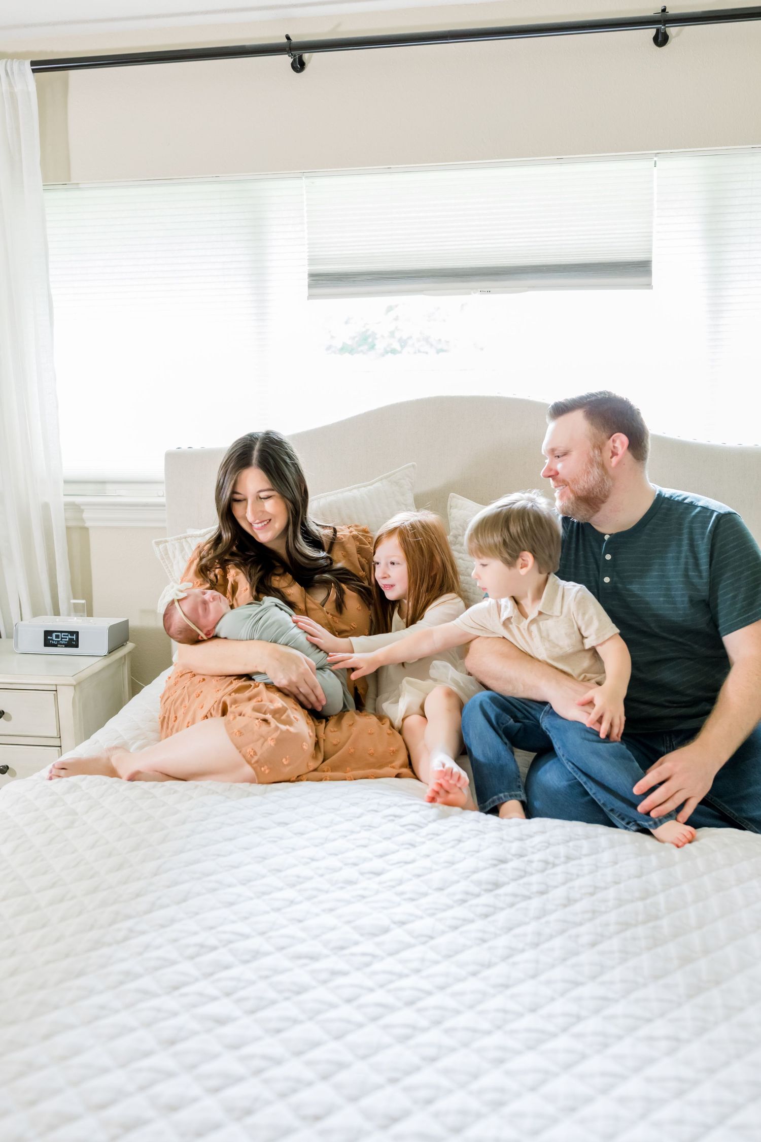 A family sits together on a white bed sharing quality time with their newborn.