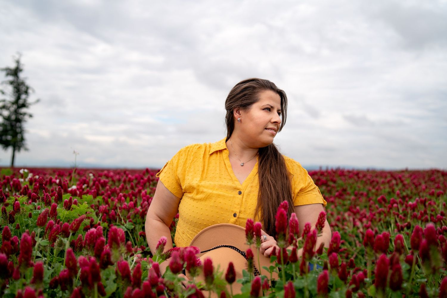 Portrait of photographer in yellow shirt holding hat in a crimson clover field in Oregon