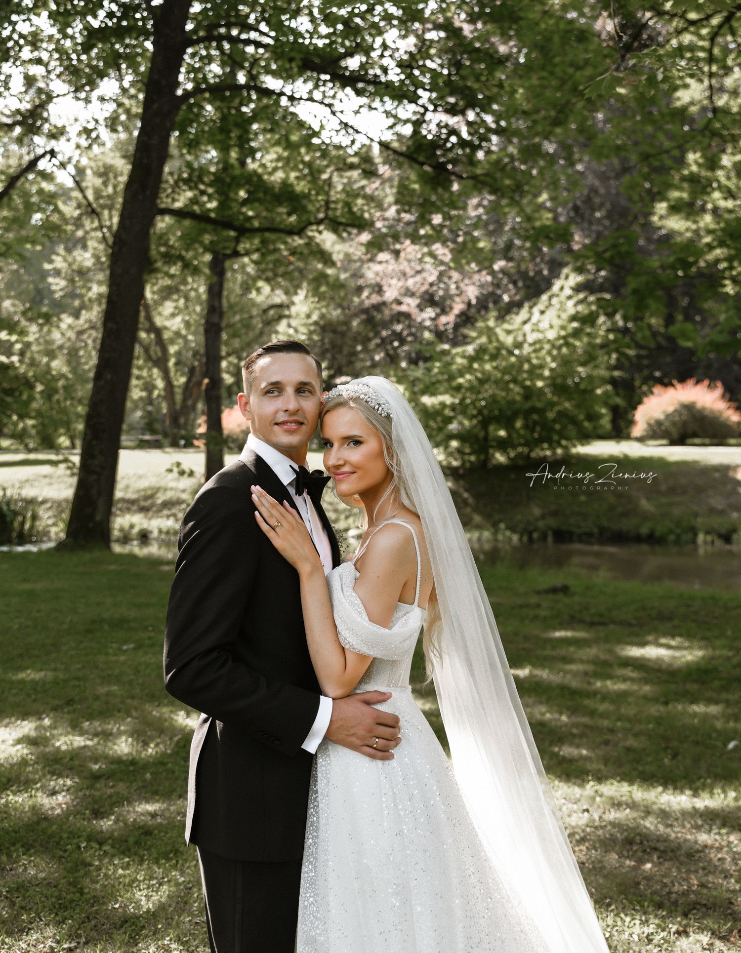 Newlyweds pose together in garden setting with natural lighting filtering through trees.