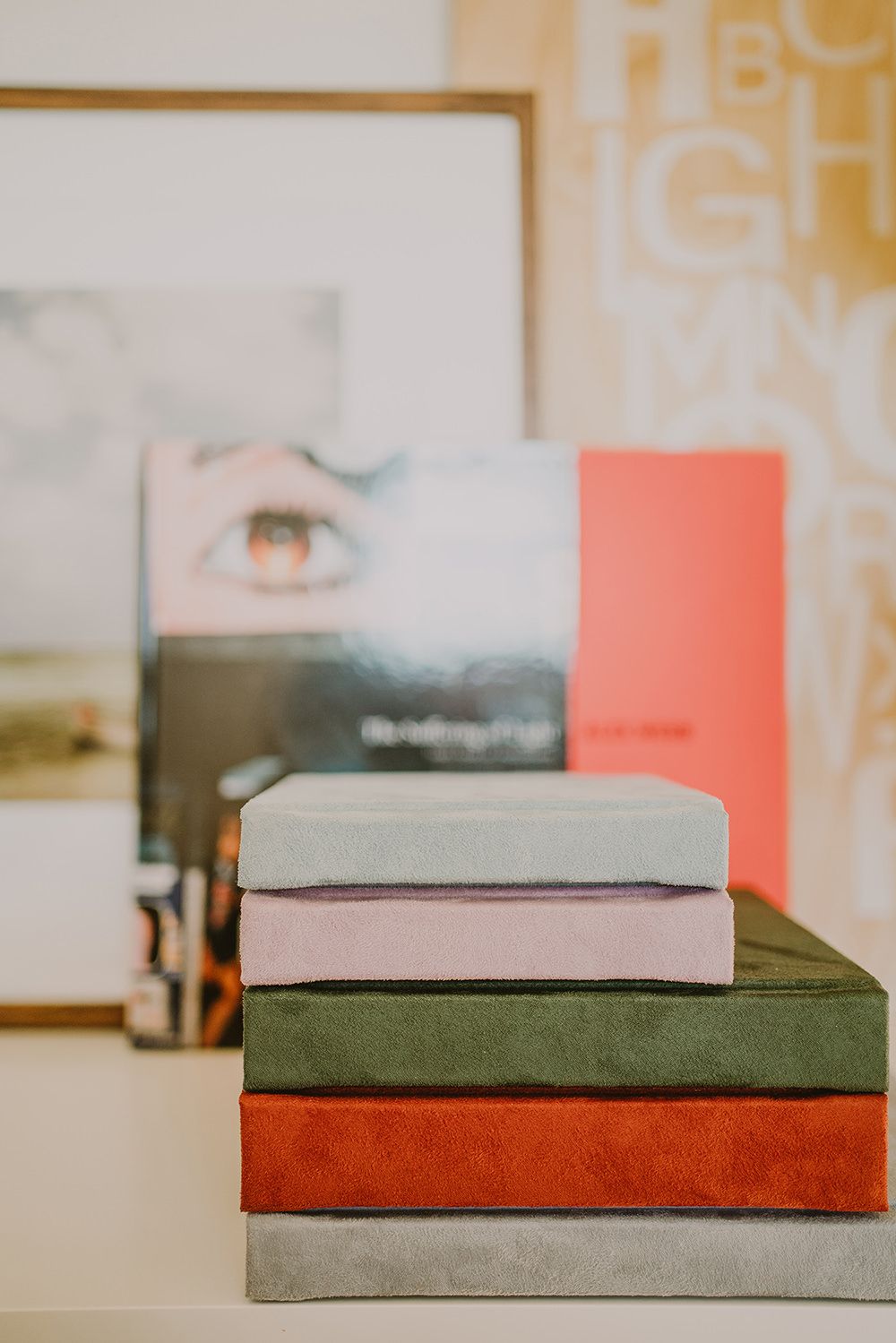 Stack of velvet-bound books in pastel and earth tones against a bright background.