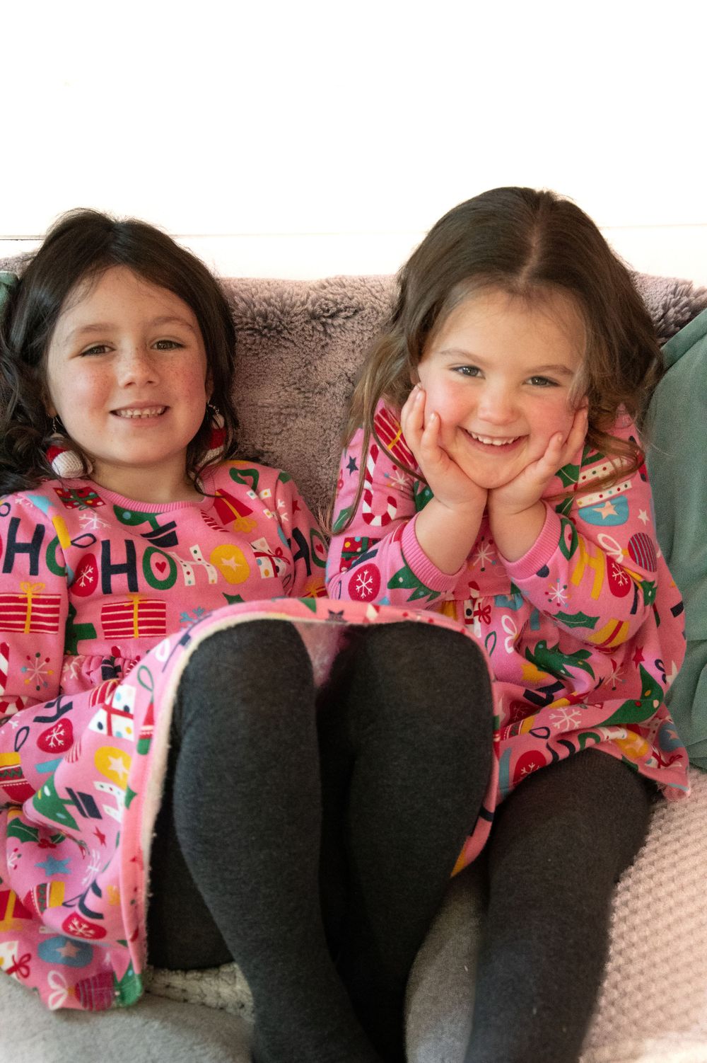 Two children wearing matching pink patterned pajamas sitting together on a couch.
