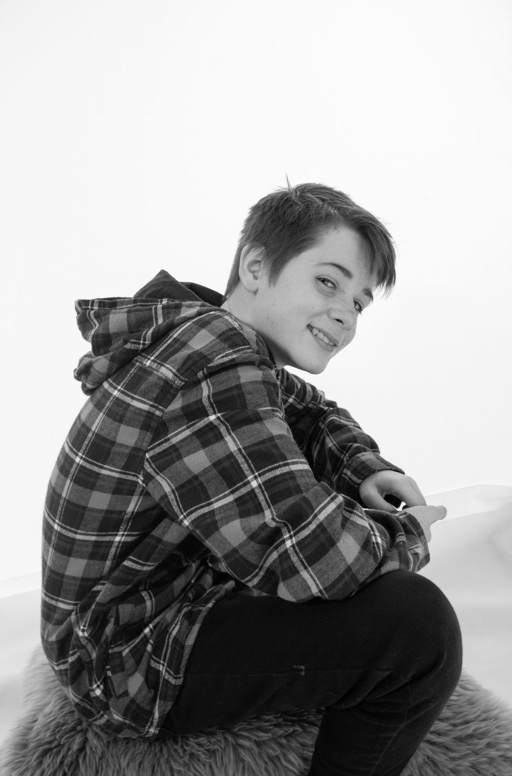 Person in plaid hoodie sits sideways on furry surface against white background.