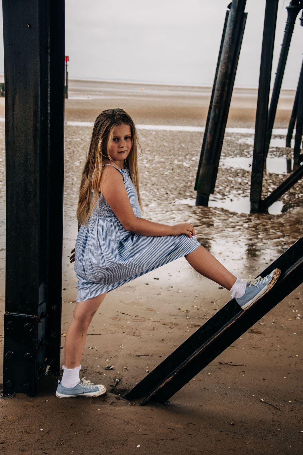A summer beach photo under a pier showing someone in a striped dress and sneakers.