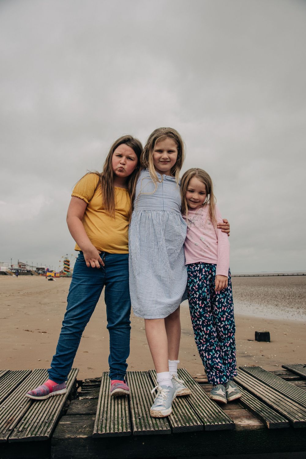 Three people stand together on wooden boardwalk at the beach on cloudy day.