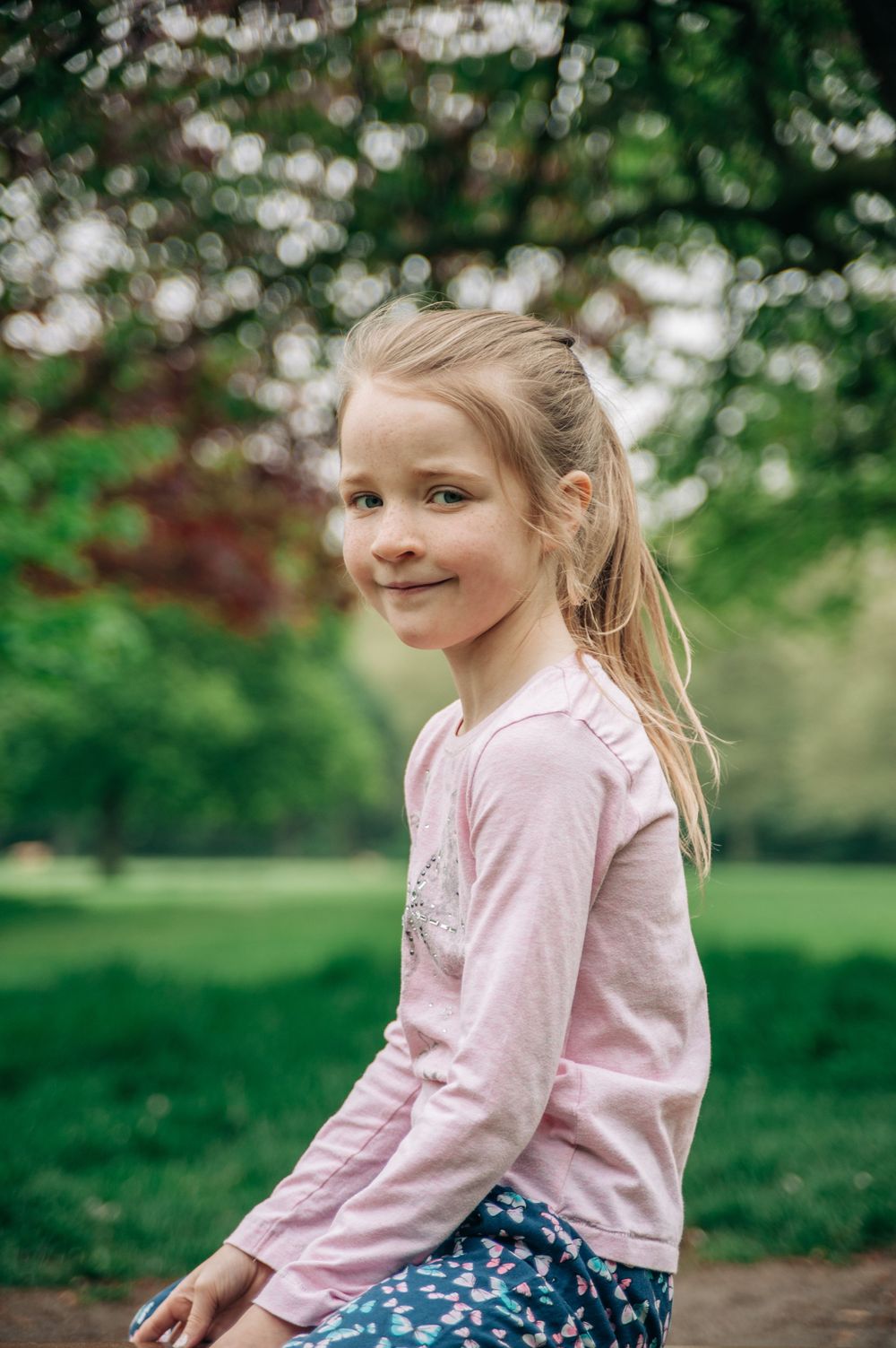A child in a pink sweater sits outdoors against a blurred nature background.