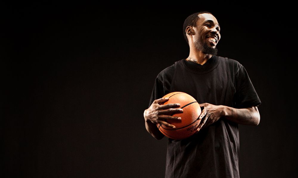 A man in a black shirt confidently holds a basketball, ready to make a move on the court.