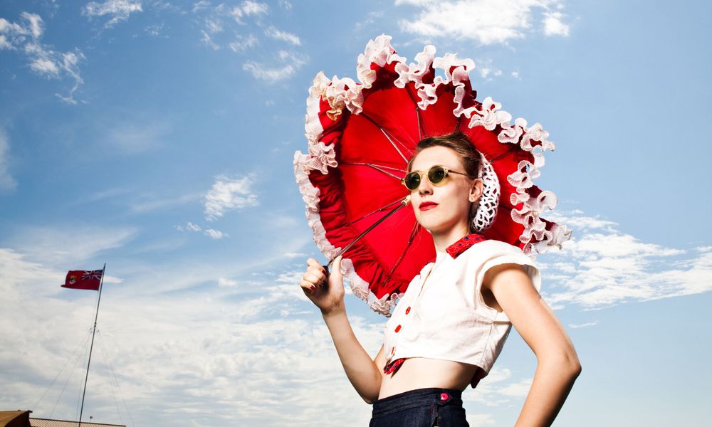 Woman holding red umbrella in sunny weather, looking up with a smile.