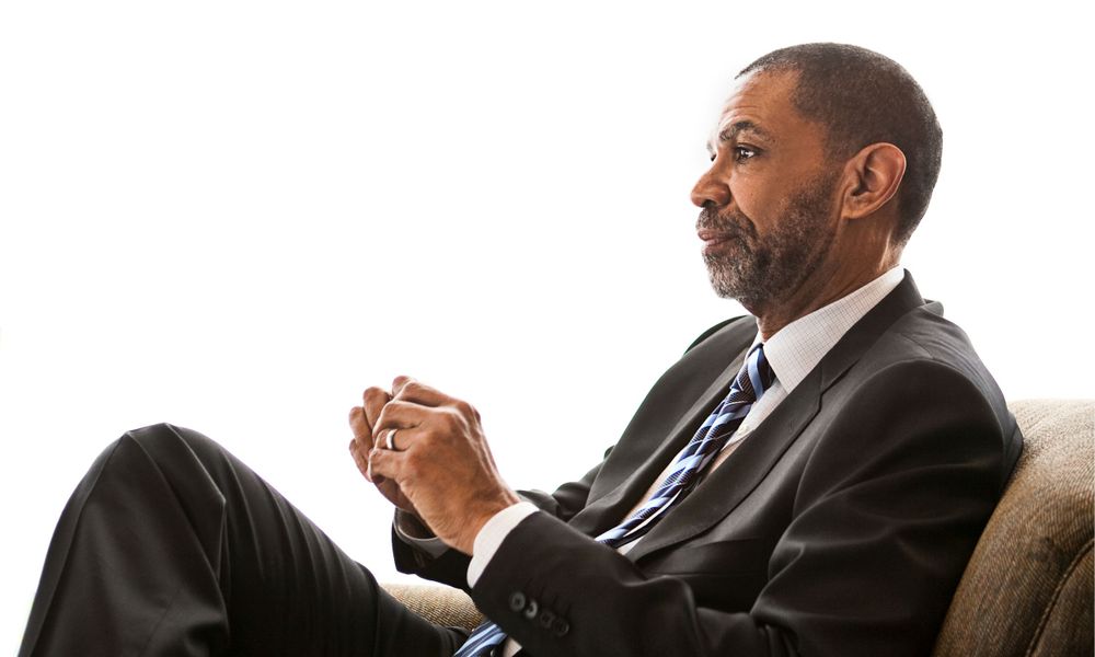 Businessman in suit and tie sitting on couch.