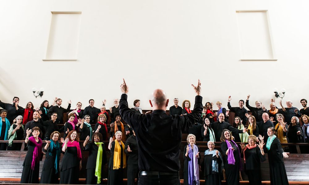 A choir singing in colorful scarfs in a church with a man leading the group. Harmonious voices fill the sacred space.