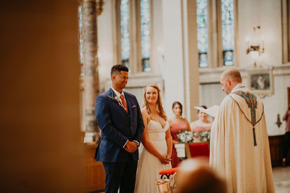Bride and groom holding hands at the altar with officiant during church wedding ceremony.