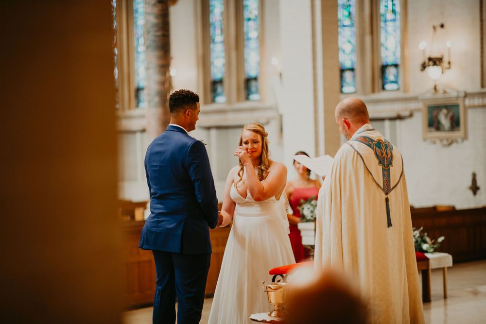 Bride and groom holding hands while officiant reads during elegant church wedding ceremony.