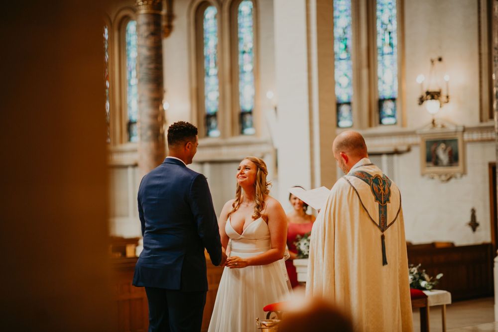 Bride gazes lovingly at groom while holding hands during church wedding ceremony.