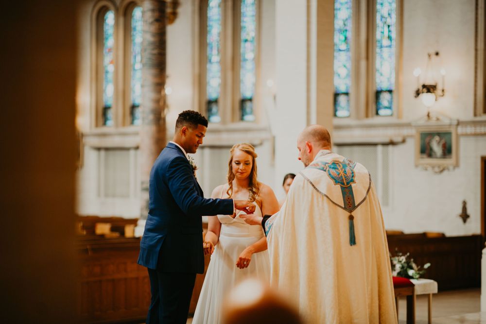 Bride and groom exchange vows at church altar with priest in ornate vestments during wedding ceremony.