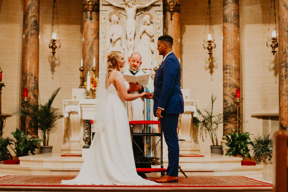 Couple stands at grand church altar with crucifix backdrop as officiant presides over wedding ceremony.