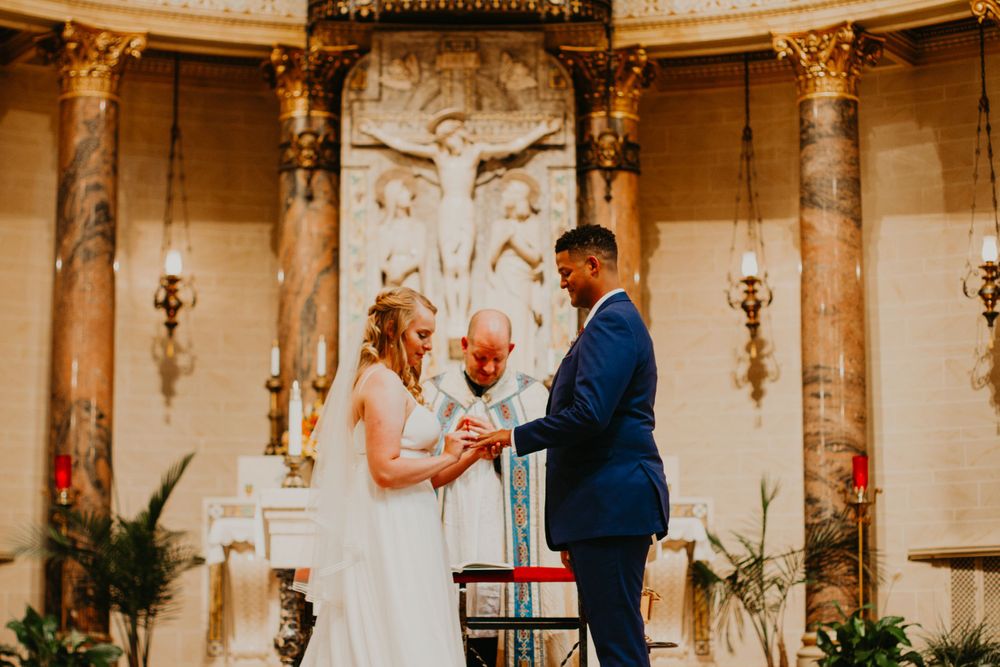 Bride and groom exchange rings at church altar during wedding ceremony with crucifix backdrop.