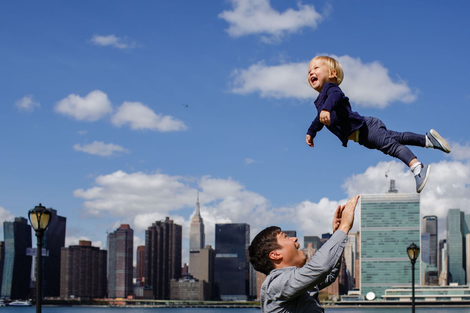 A playful moment against the NYC skyline as a child is lifted high into the air.