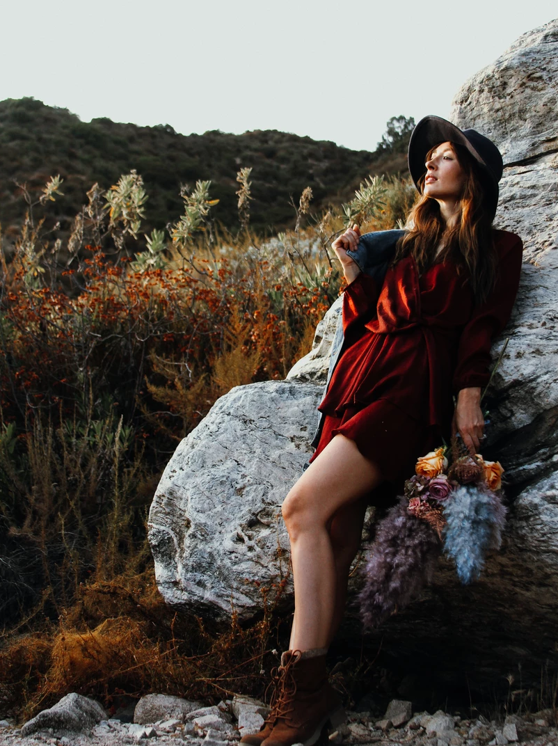 Fashion portrait on rocky terrain with red dress and autumn foliage.