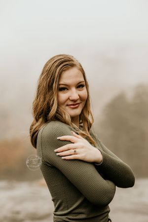 Person in olive sweater smiling warmly against a soft neutral background.