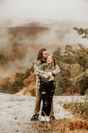 Couple sitting together on rocky terrain with misty mountains in background.
