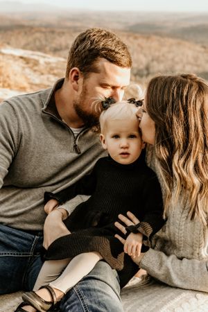 Candid family moments captured in warm tones as parents share affection with their young child.