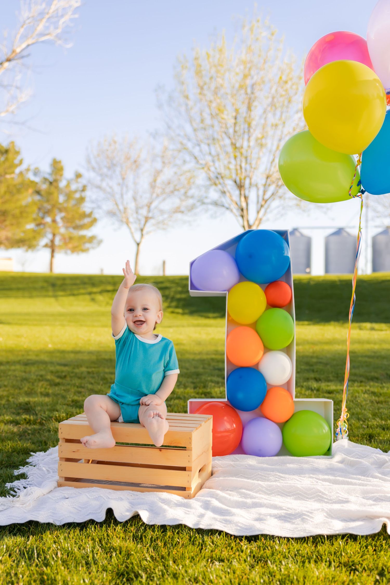 Baby on wooden crate next to balloon number one display outdoors.