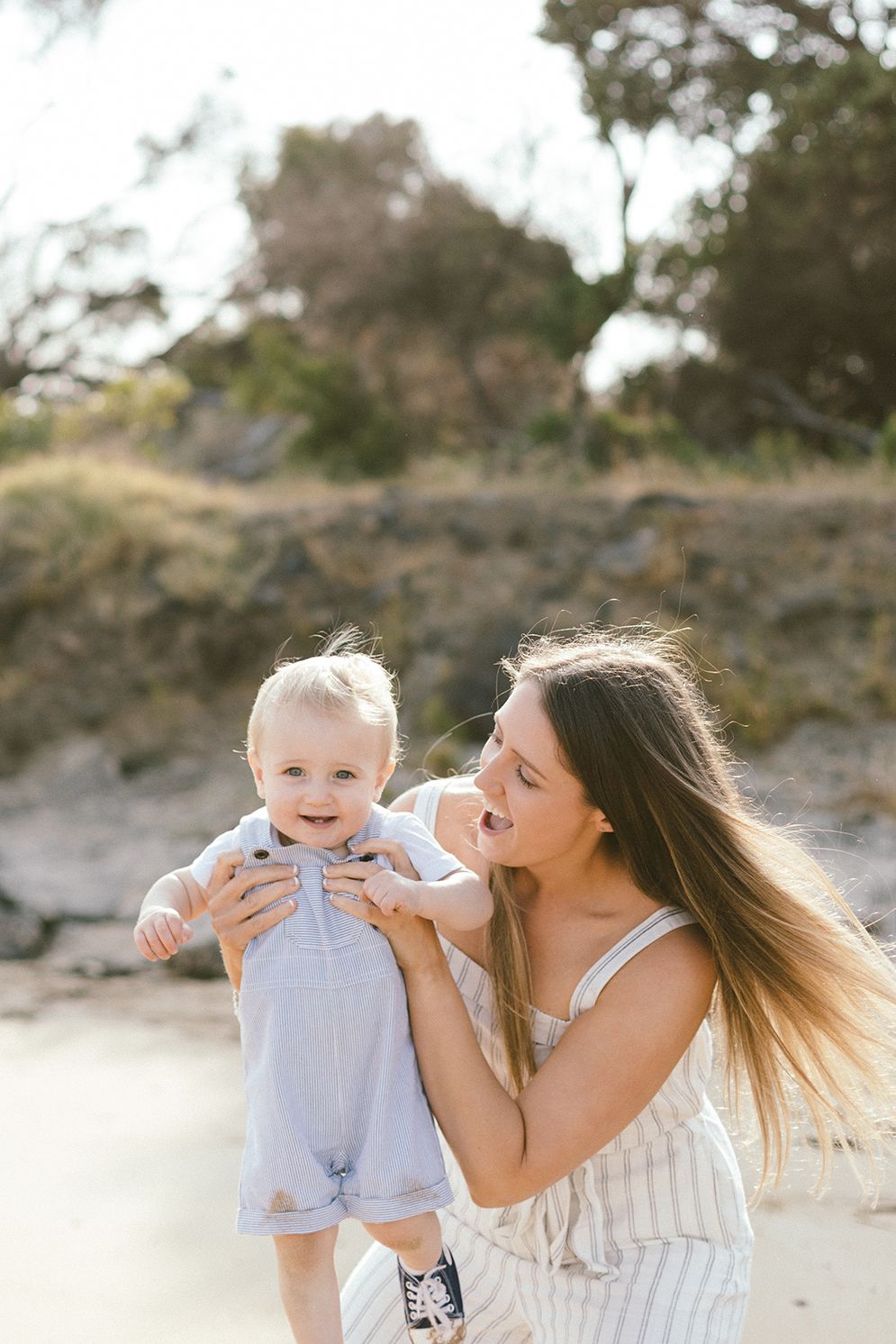 A tender family moment captured on a sandy beach with natural scenery.
