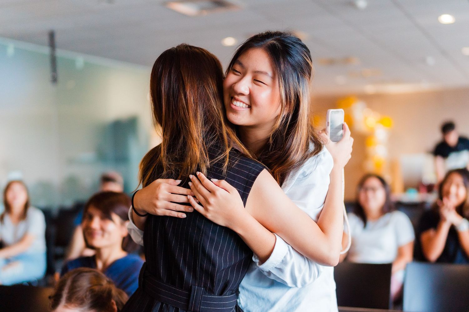 Two people sharing an emotional embrace during a celebration while others watch in the background.