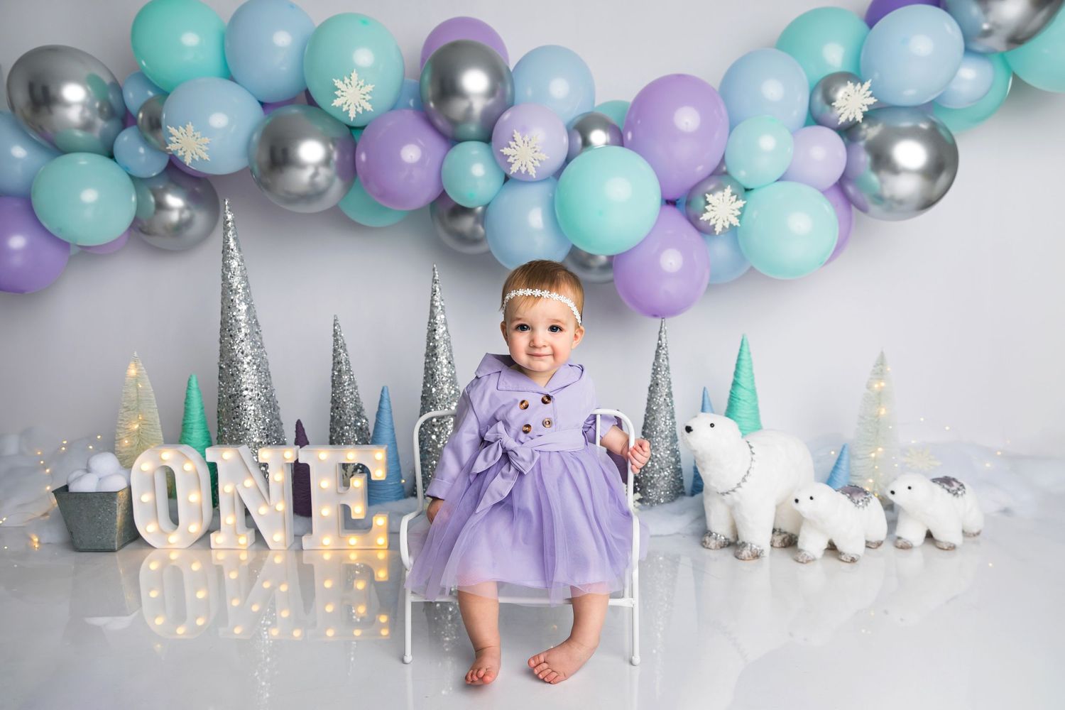 First birthday celebration setup with purple and blue balloons, silver decorations, and white unicorn figurines.