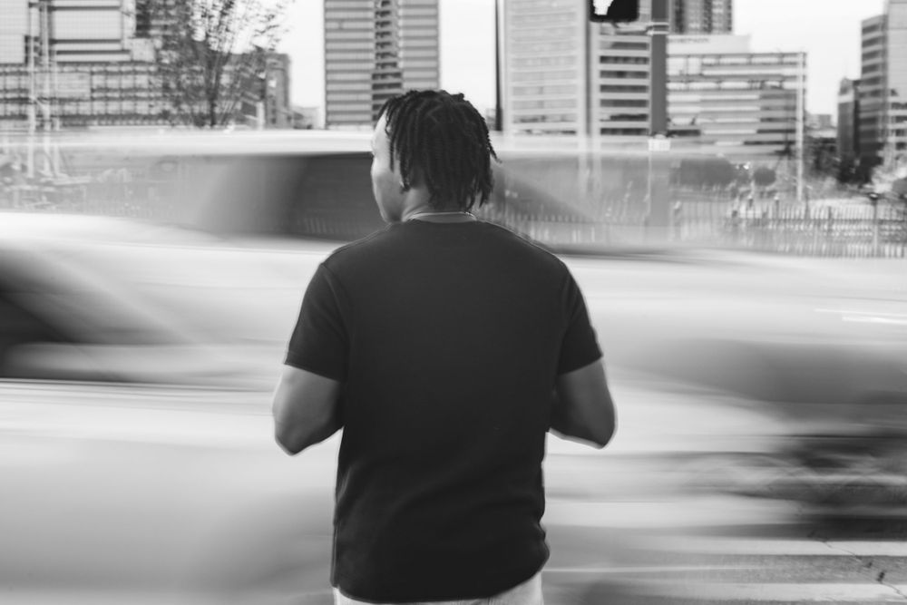 Blurred motion shot of person in black shirt standing against urban backdrop.