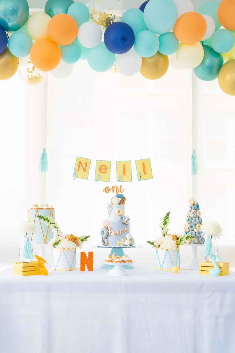 a vertical view of a birthday table with cake and treats with a musical theme in light blue, aqua and orange colors