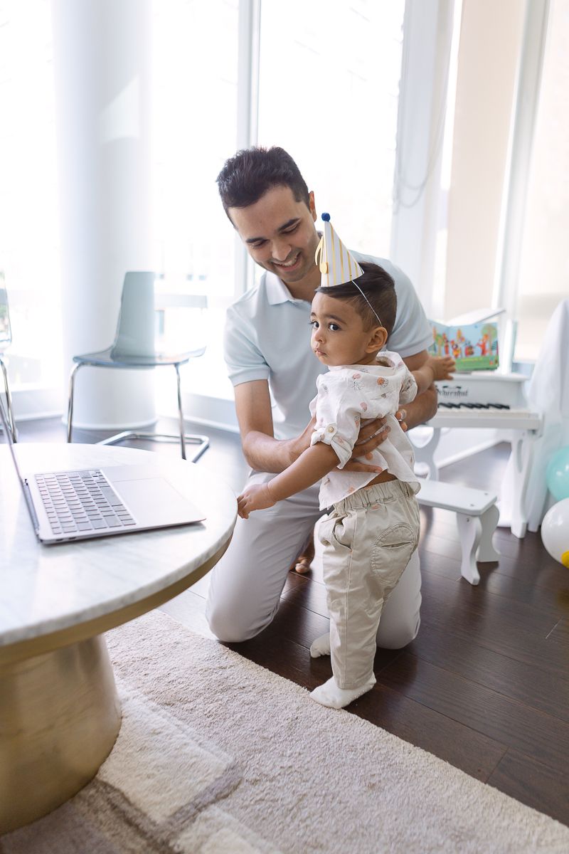 a father and one year old son stand in front of a laptop during a zoom birthday party in Hoboken photo by Paula Ortiz