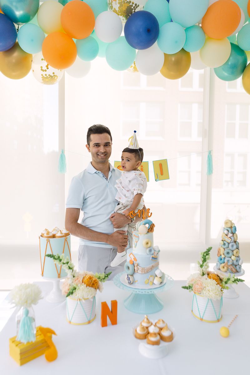 a portrait view of a father holding his son behind the birthday table decor with a bright background photo by Paula O