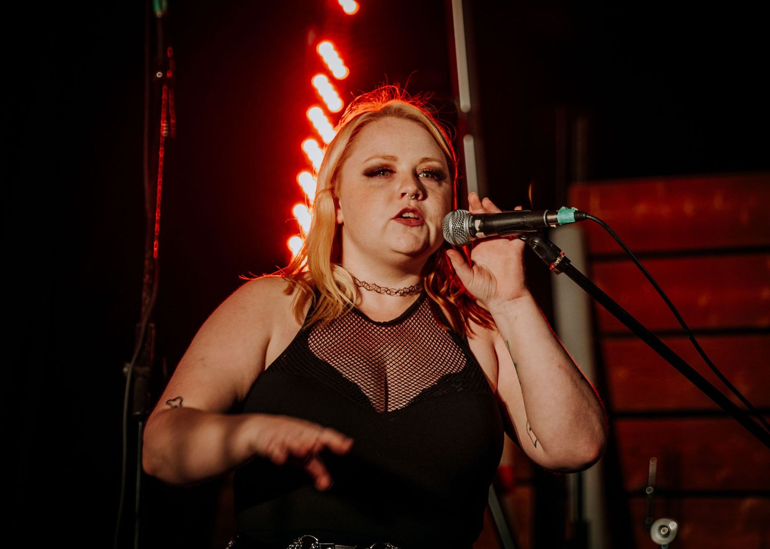 A rock singer in black mesh top performs energetically against a red-lit backdrop.