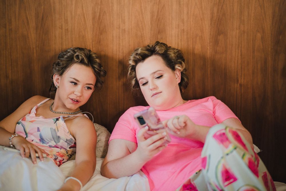 Two friends relaxing together on a couch while looking at their phones.