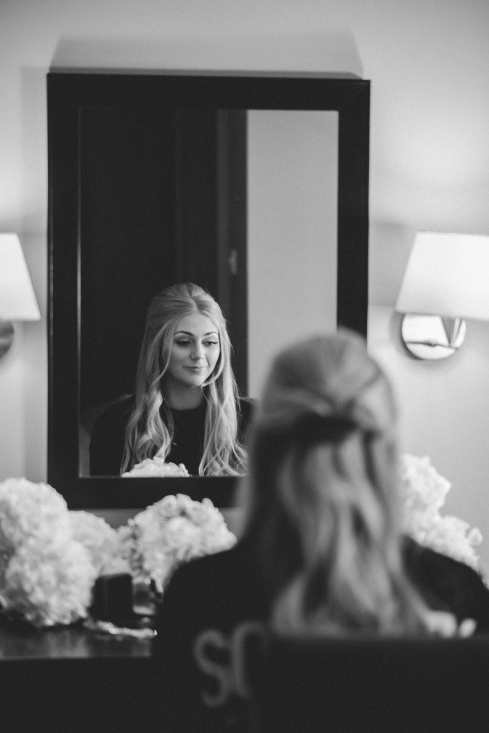 A reflection in a vanity mirror shows someone getting ready with styled blonde hair.
