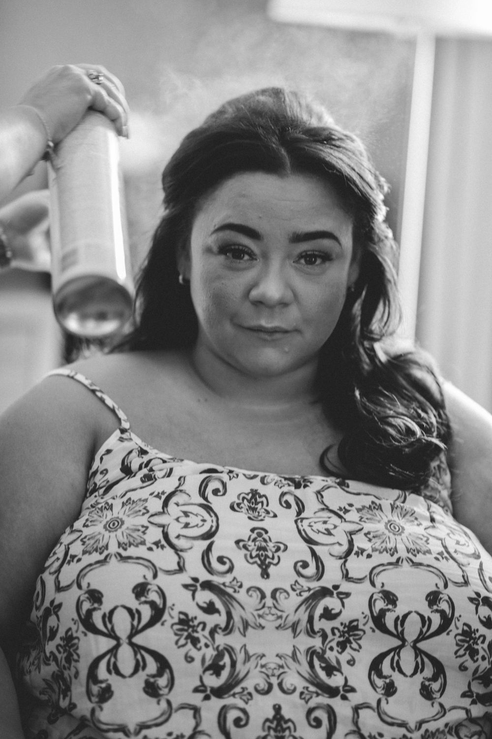Someone sprays hairspray while wearing a patterned white and black dress during preparation.