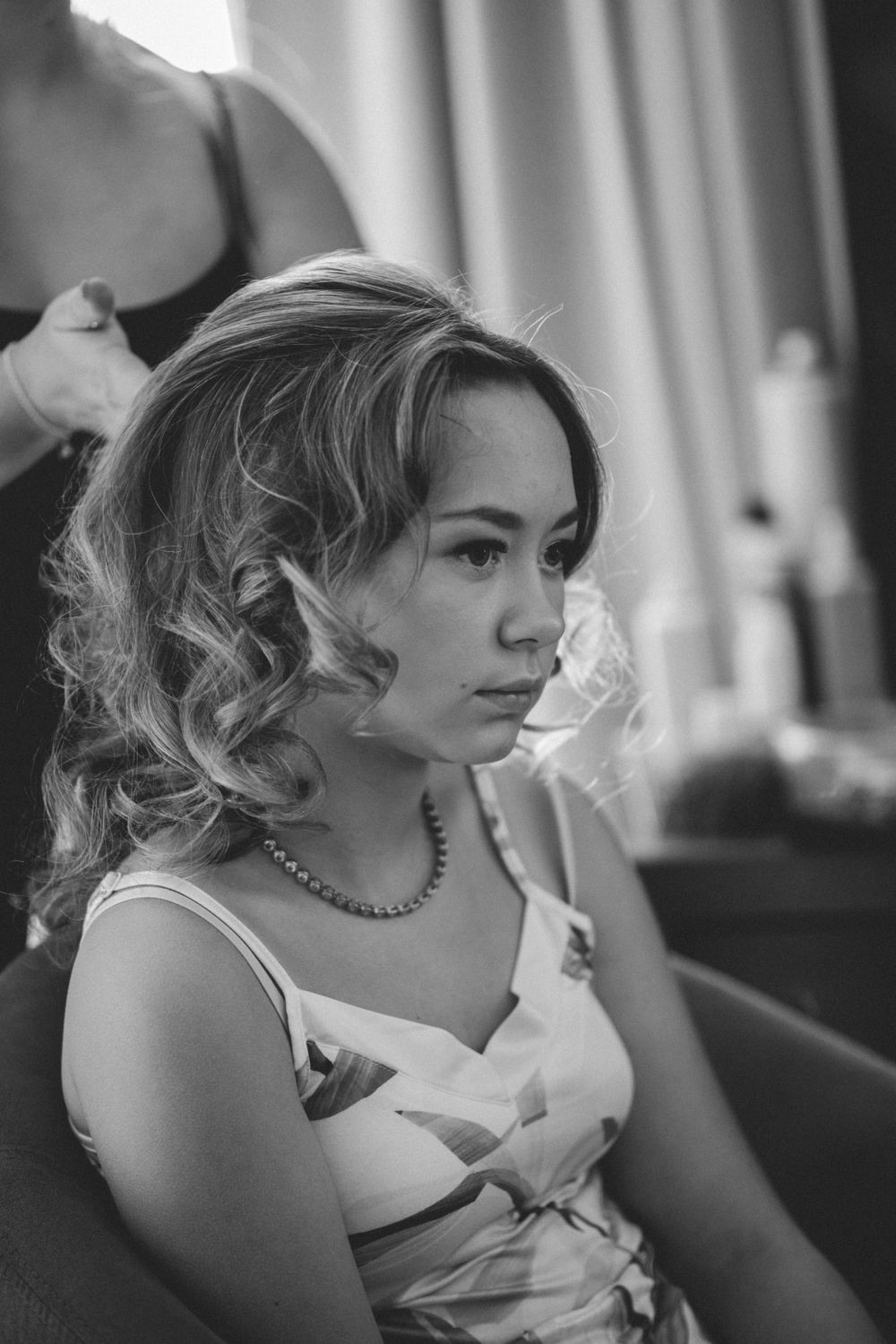 Black and white portrait of someone in an elegant white dress with curled hair and jewelry.