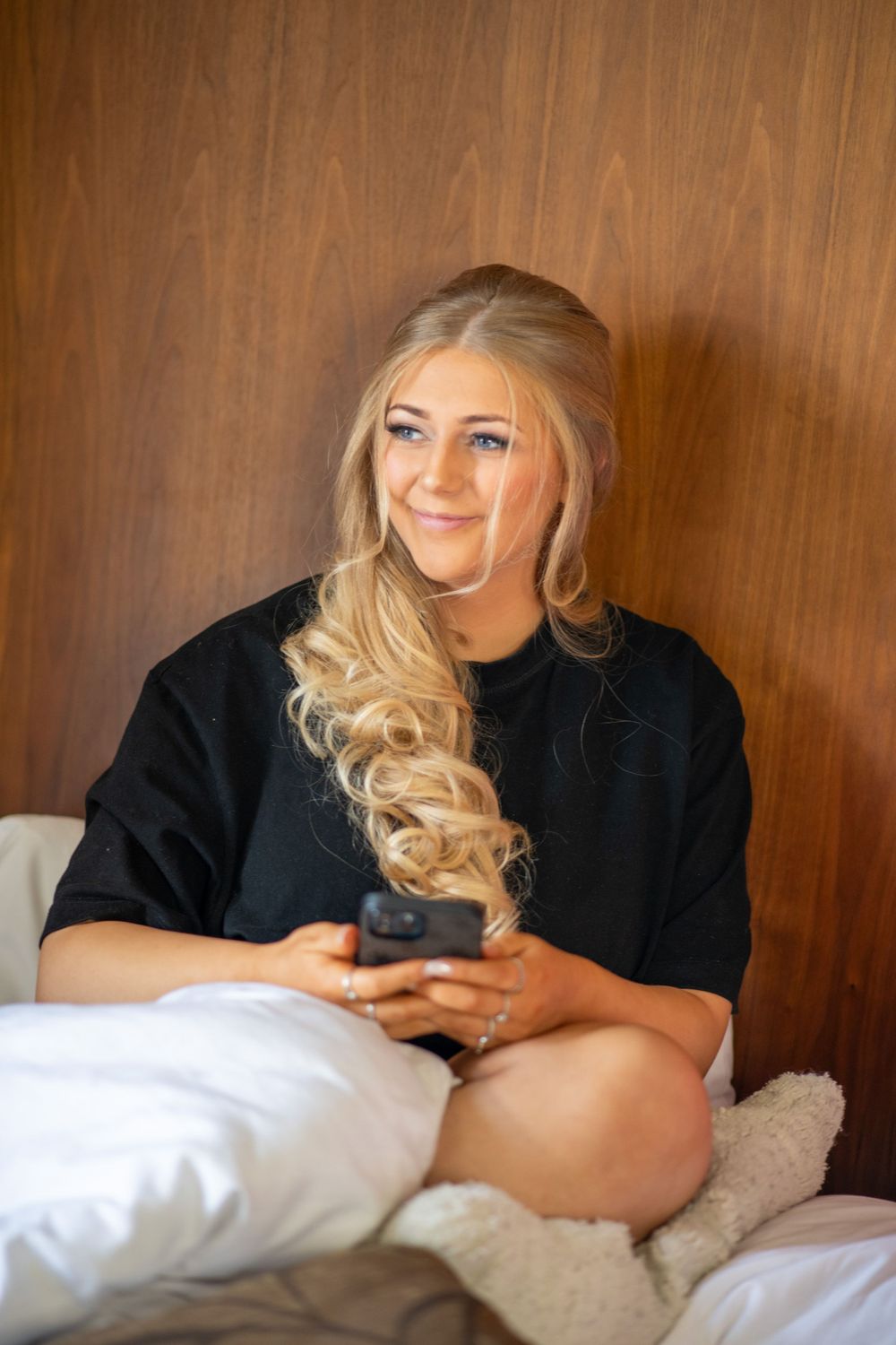A person in black relaxes on white bedding while looking to the side with a gentle smile.