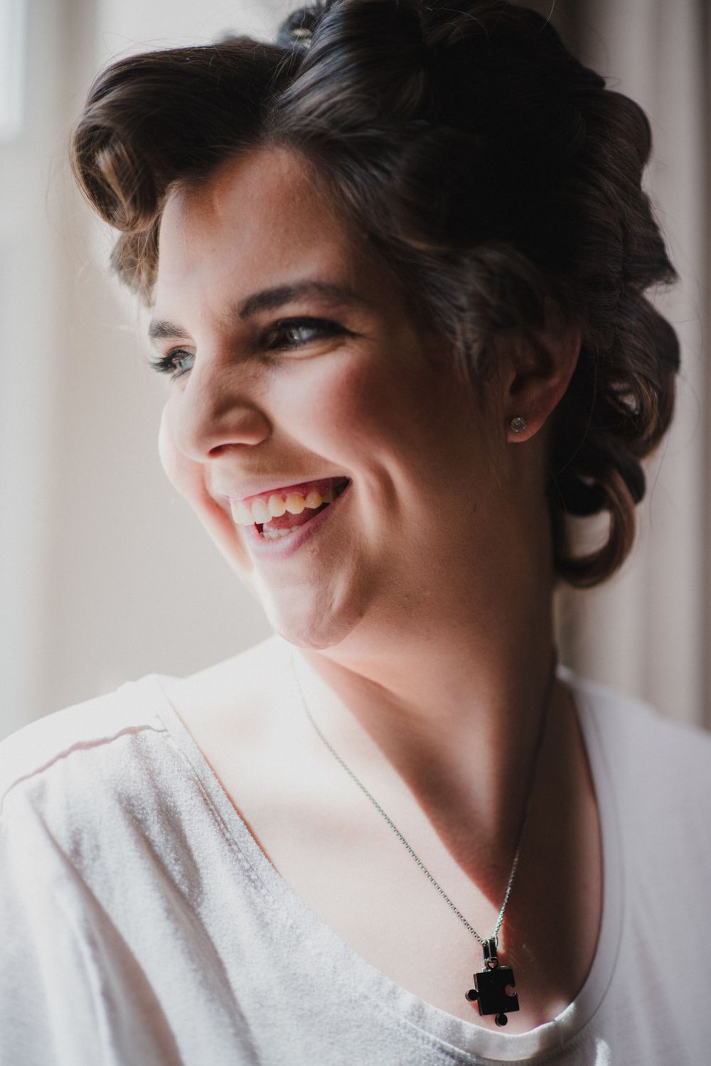 Portrait of someone smiling and wearing a white top with a black pendant necklace.