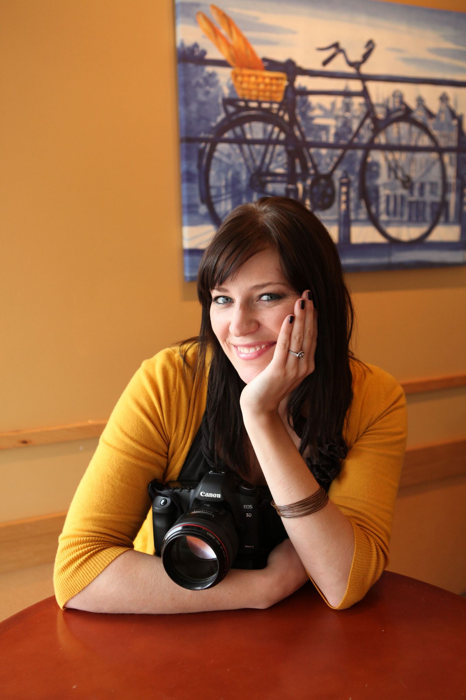 Photographer with camera posing against orange wall with bicycle artwork.
