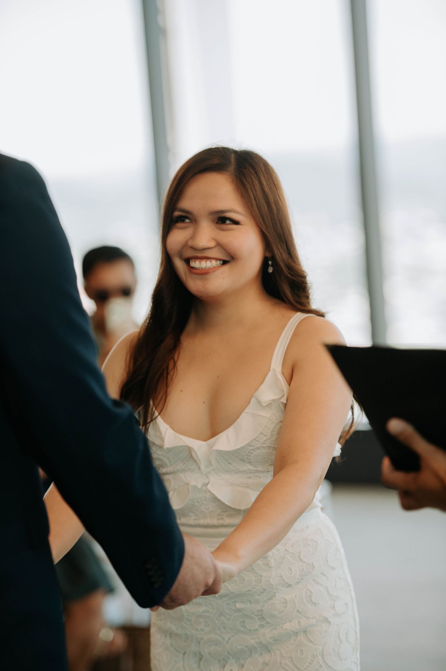 Bride wearing a white lace dress smiles during wedding ceremony.