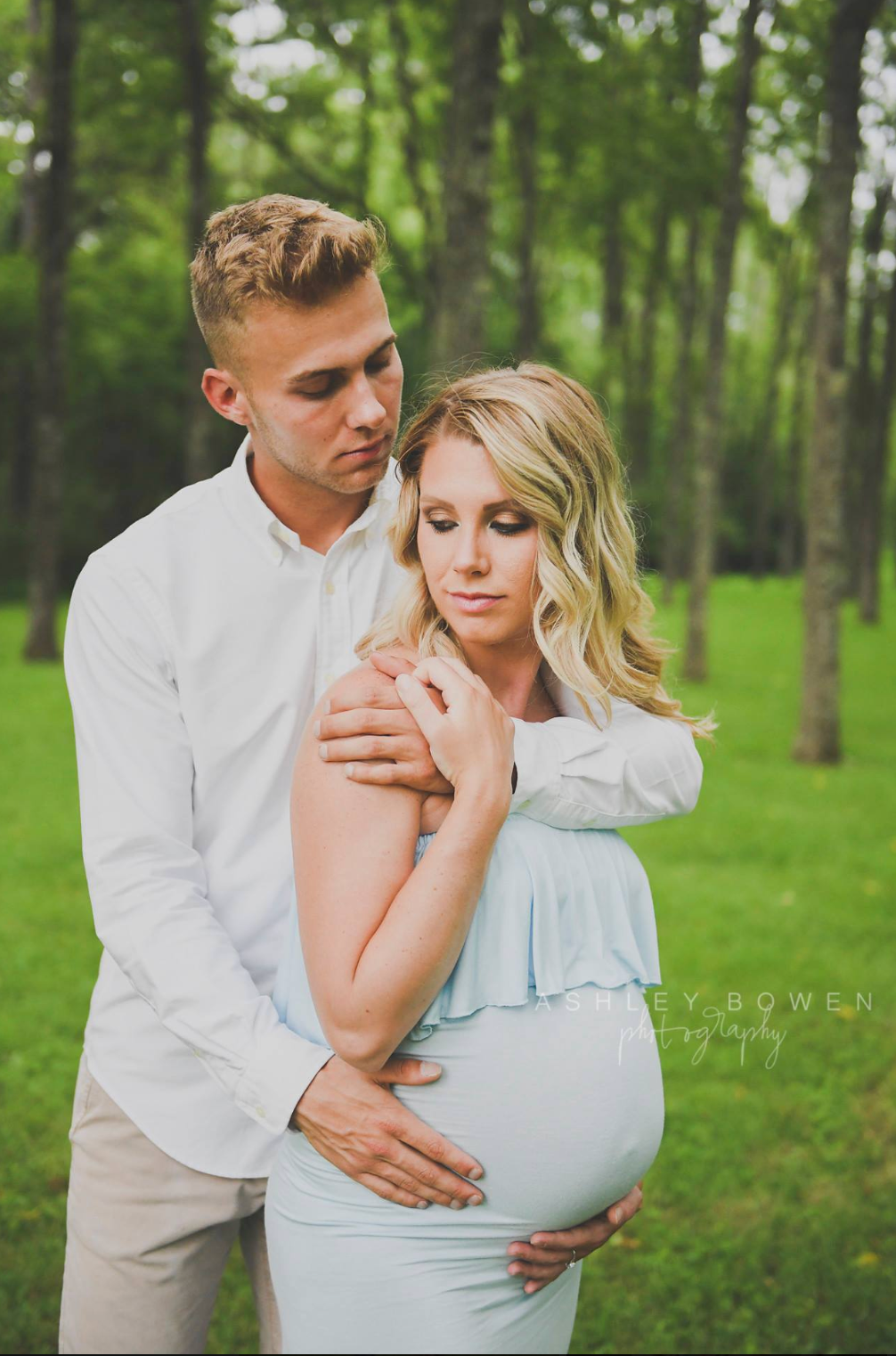 Expecting couple embracing tenderly in green forest during outdoor maternity photo session.