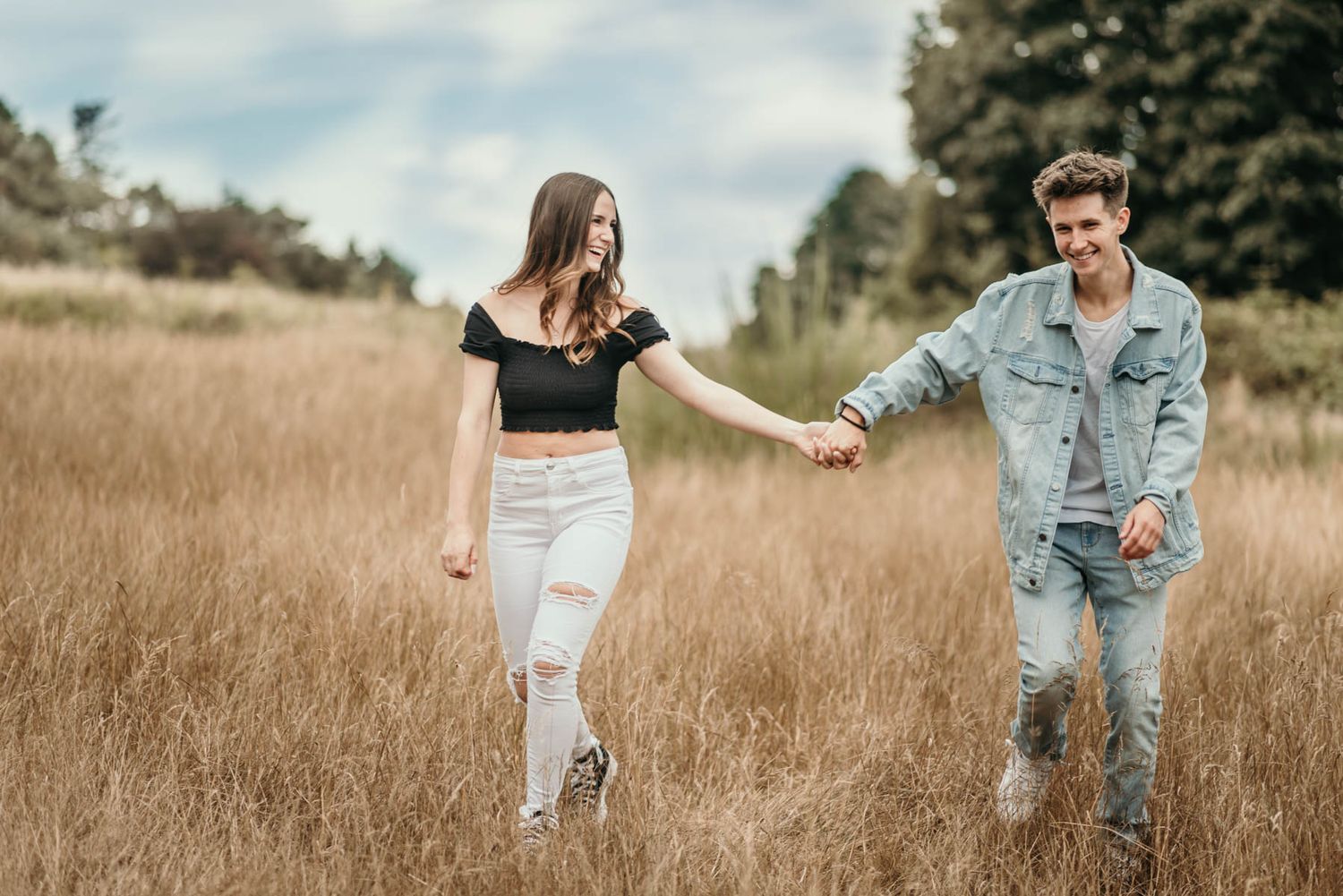 A couple walks hand in hand through a golden wheat field on a sunny afternoon.