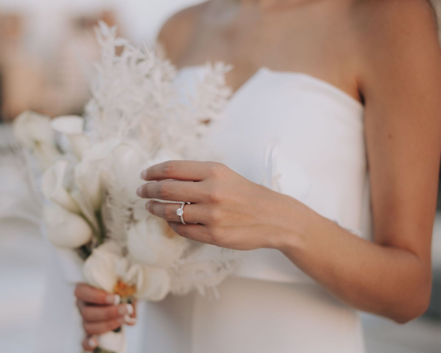 Elegant bridal details showing white dress, engagement ring, and delicate bouquet.