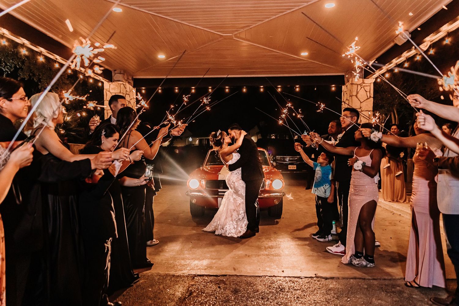 Newlyweds sharing a kiss during sparkler exit surrounded by cheering wedding guests at night taken by Houston Wedding Photographer.