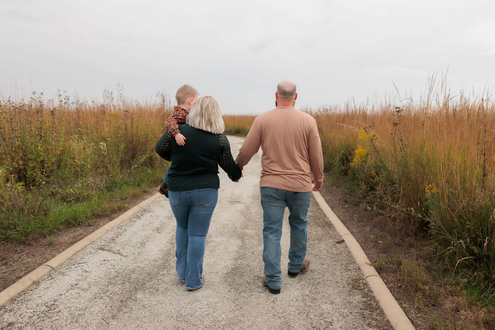 A couple walks hand in hand down a gravel path surrounded by tall autumn grasses.