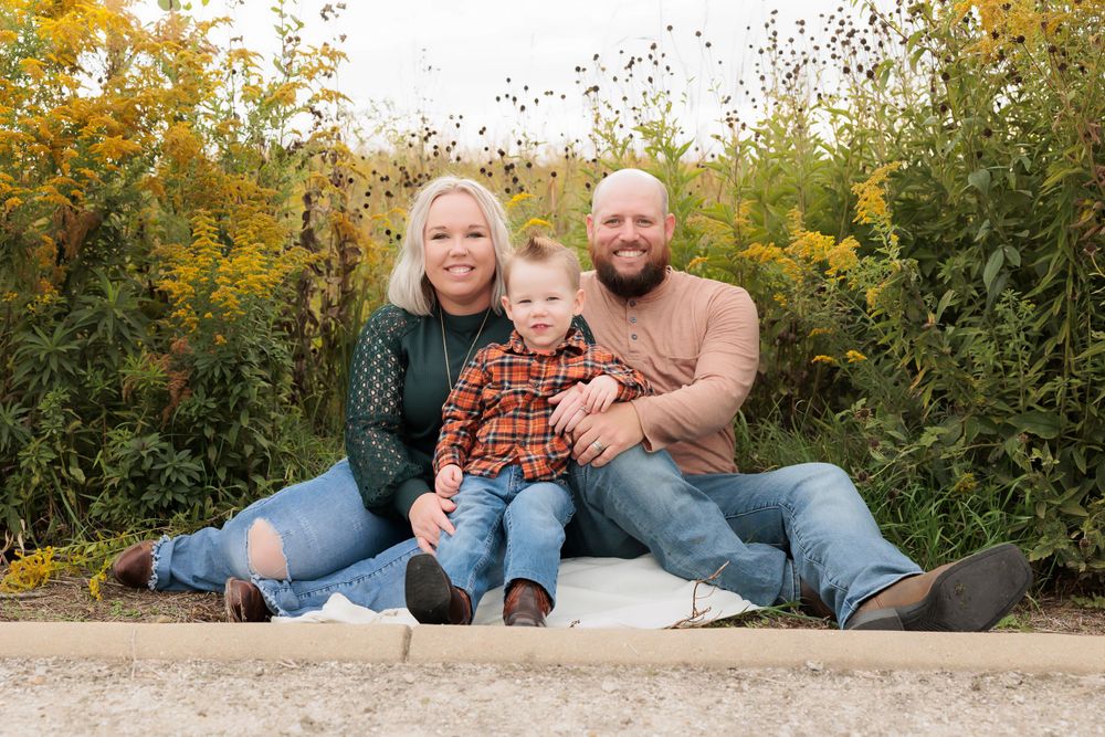 Family sitting together on white blanket with yellow wildflowers in background.