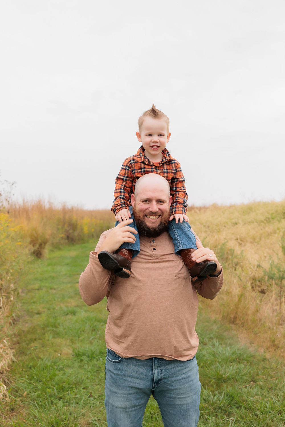 A loving moment shared on a grassy path with a child perched on shoulders on an autumn day.