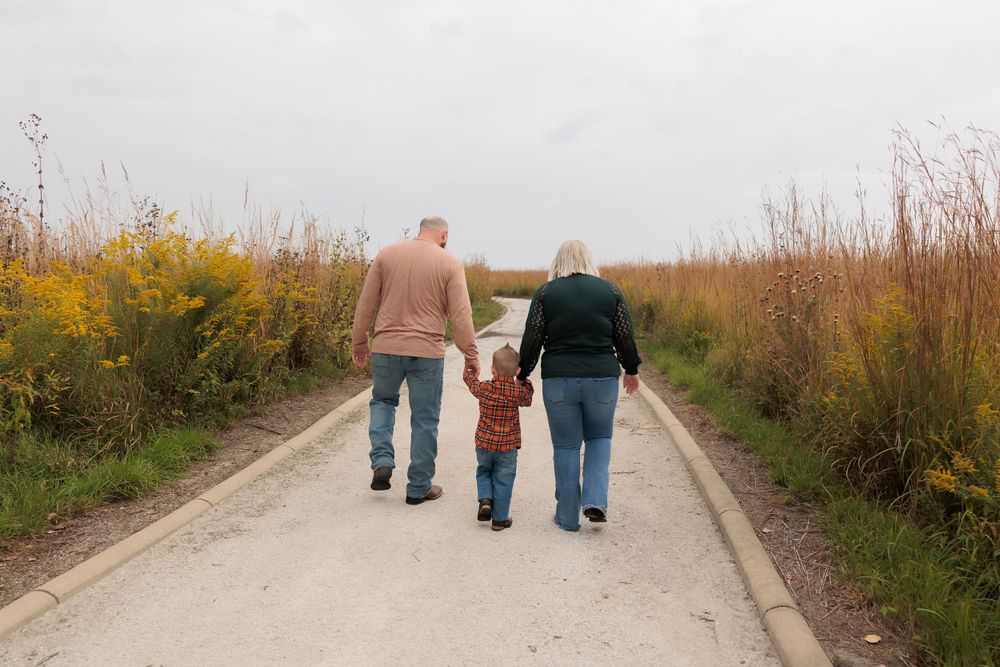Three people walking hand in hand down a path surrounded by autumn wildflowers.